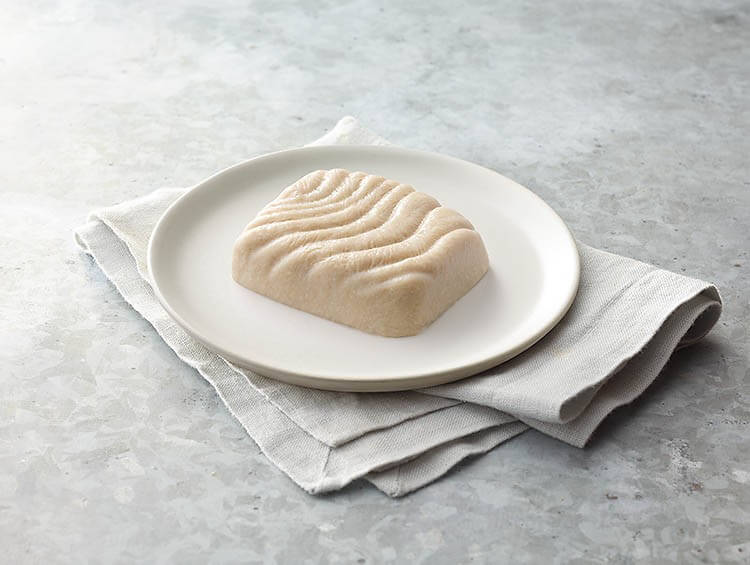 Block of fish on a white plate with a gray napkin on a light gray surface.