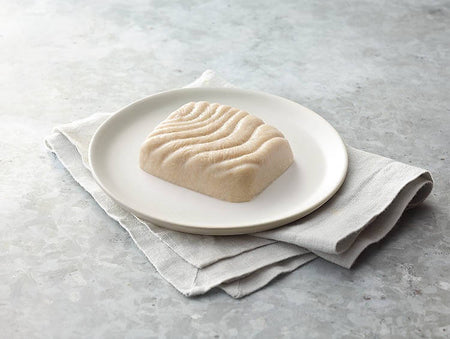 Block of fish on a white plate with a gray napkin on a light gray surface.