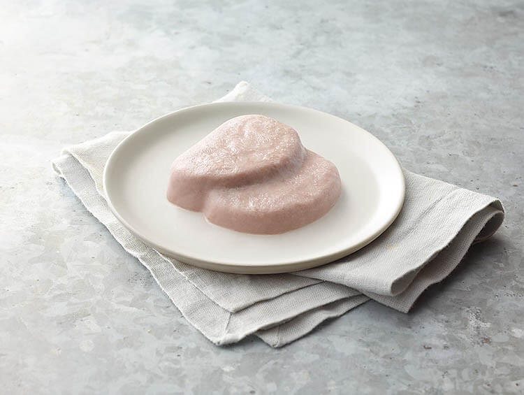 Two pieces of raw ham on a white plate with a gray napkin on a light gray surface.