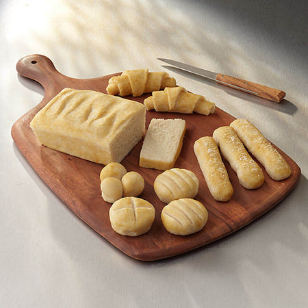 Wooden cutting board with various bread items on a light background.