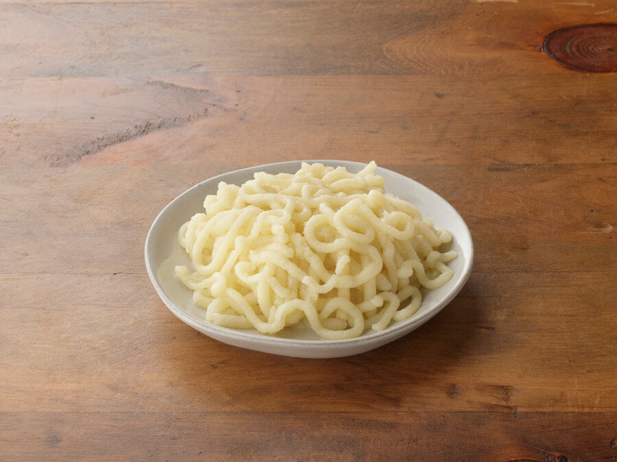 White plate with curly pasta on a wooden surface.