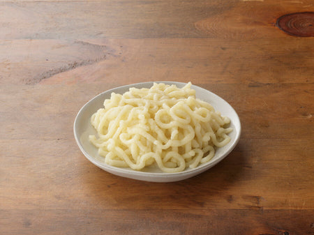 White plate with curly pasta on a wooden surface.