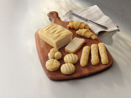 Wooden cutting board with various bread items on a light background.
