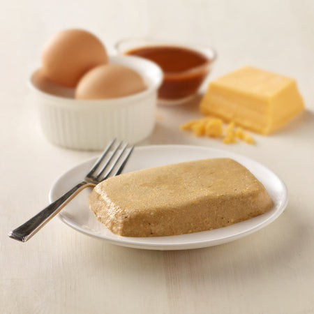 Block of brown food on a white plate with eggs, butter, and ketchup in the background.