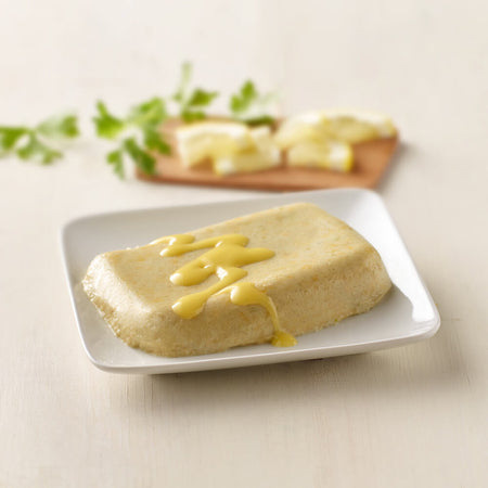 Square plate with a block of tofu drizzled with yellow sauce on a light background.