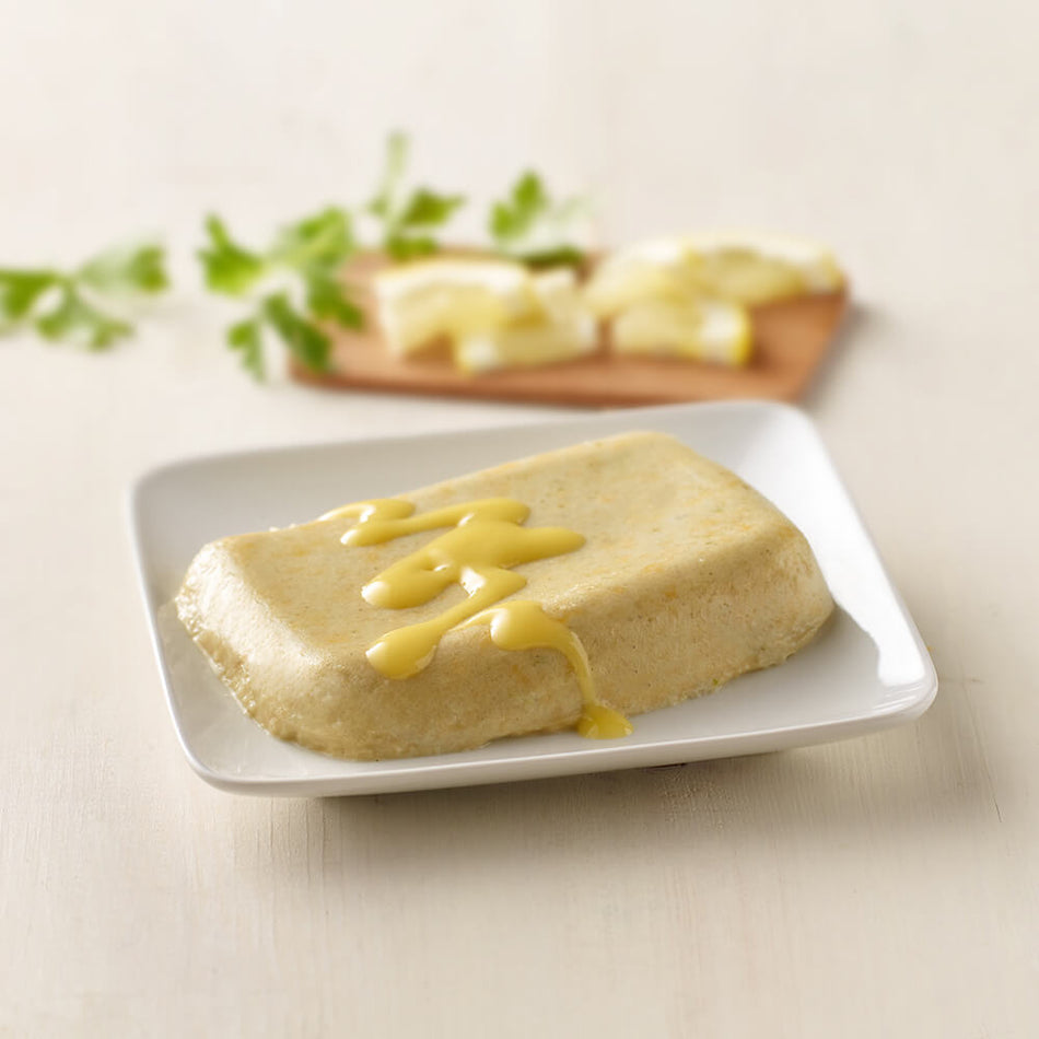 Square plate with a block of tofu drizzled with yellow sauce on a light background.
