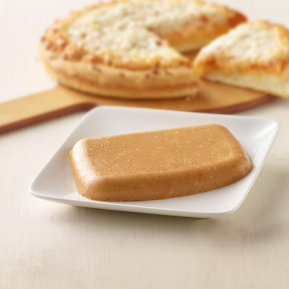 Rectangular block of brown butter on a white plate with bread in the background.