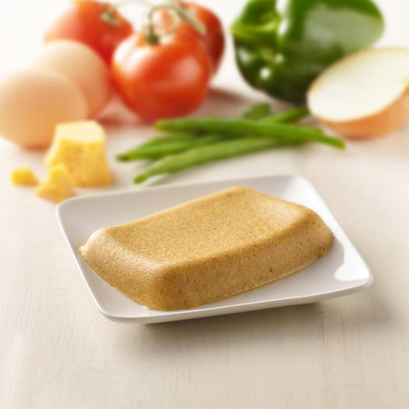 Block of vegetable on a white plate with vegetables in the background.