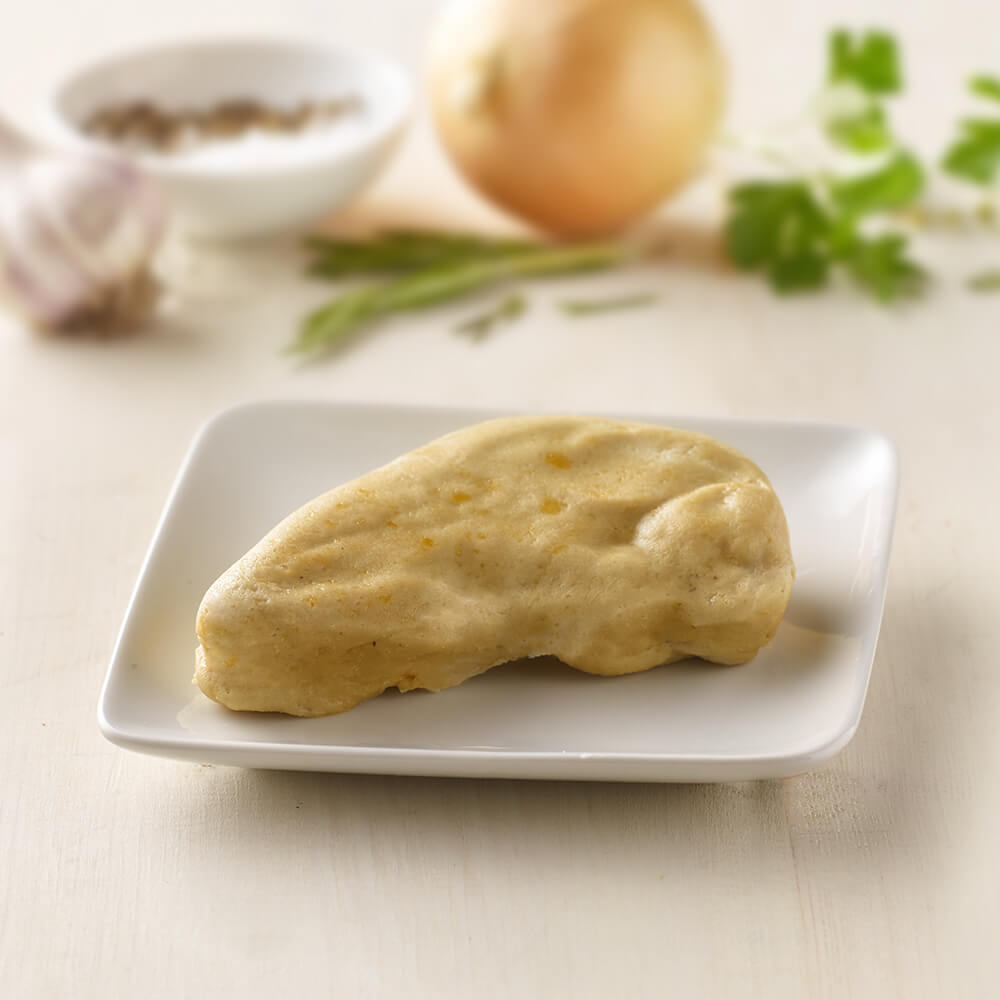 Loaf of chicken on a white plate with ingredients in the background.