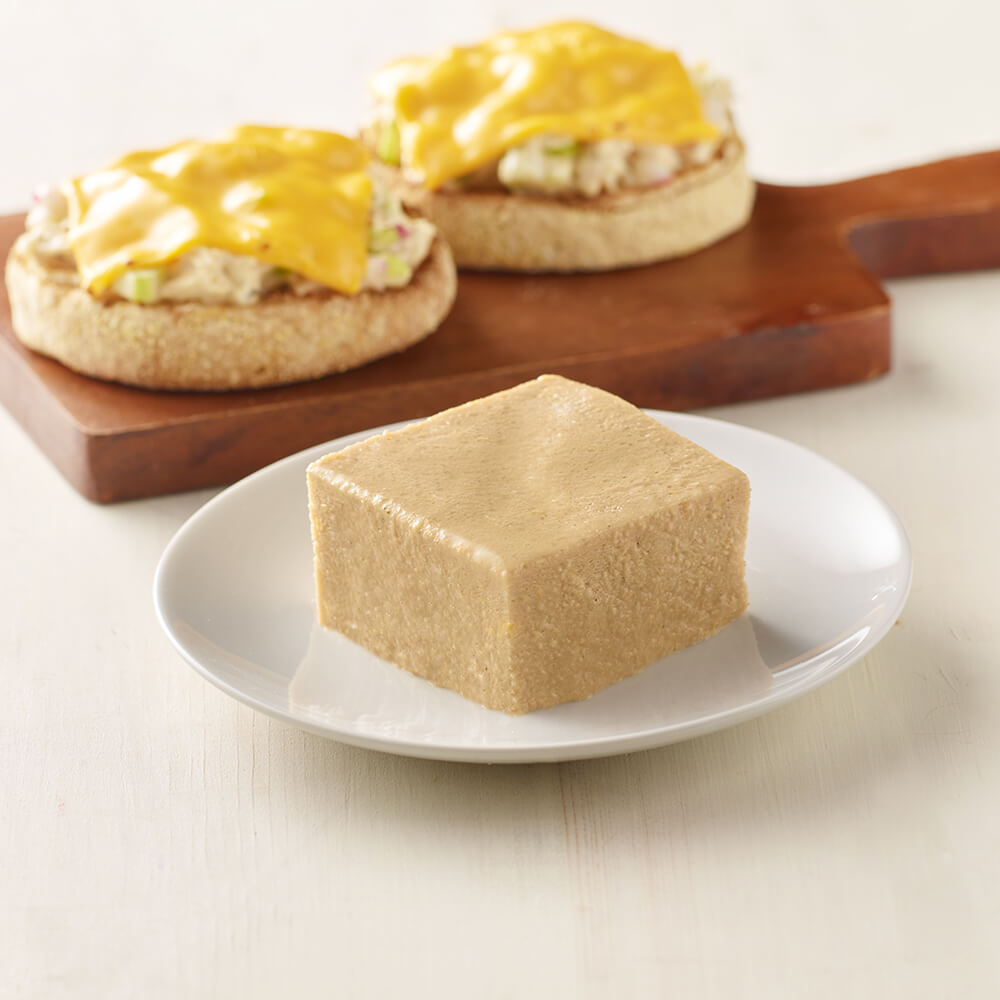 Square piece of tuna on a white plate with sandwiches in the background.