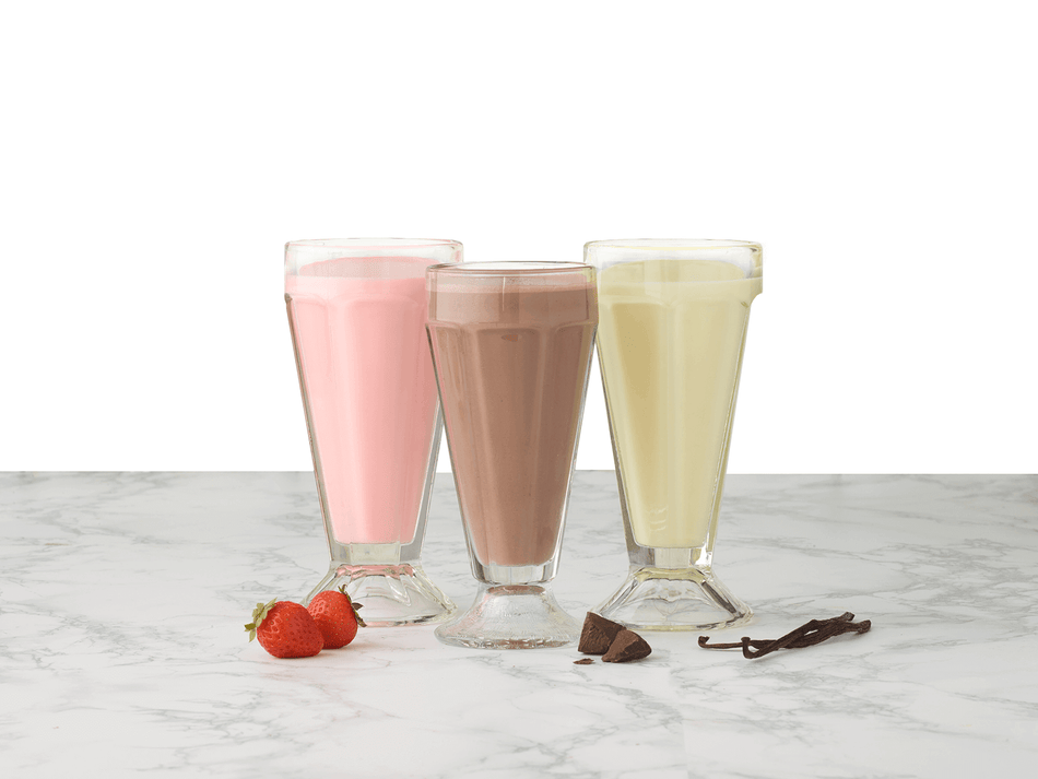 Three glasses of different flavored milkshakes on a marble surface with ingredients.