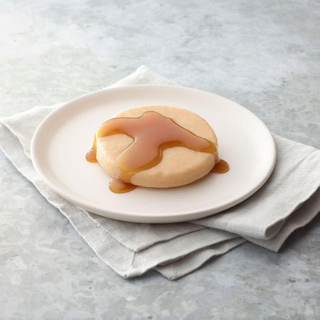 Round dessert pancake with syrup on a white plate on a light gray surface.