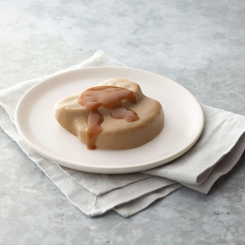 Round roast beef with caramel sauce on a white plate, placed on a light gray surface with a white napkin.