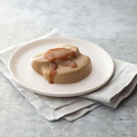 Round roast beef with caramel sauce on a white plate, placed on a light gray surface with a white napkin.
