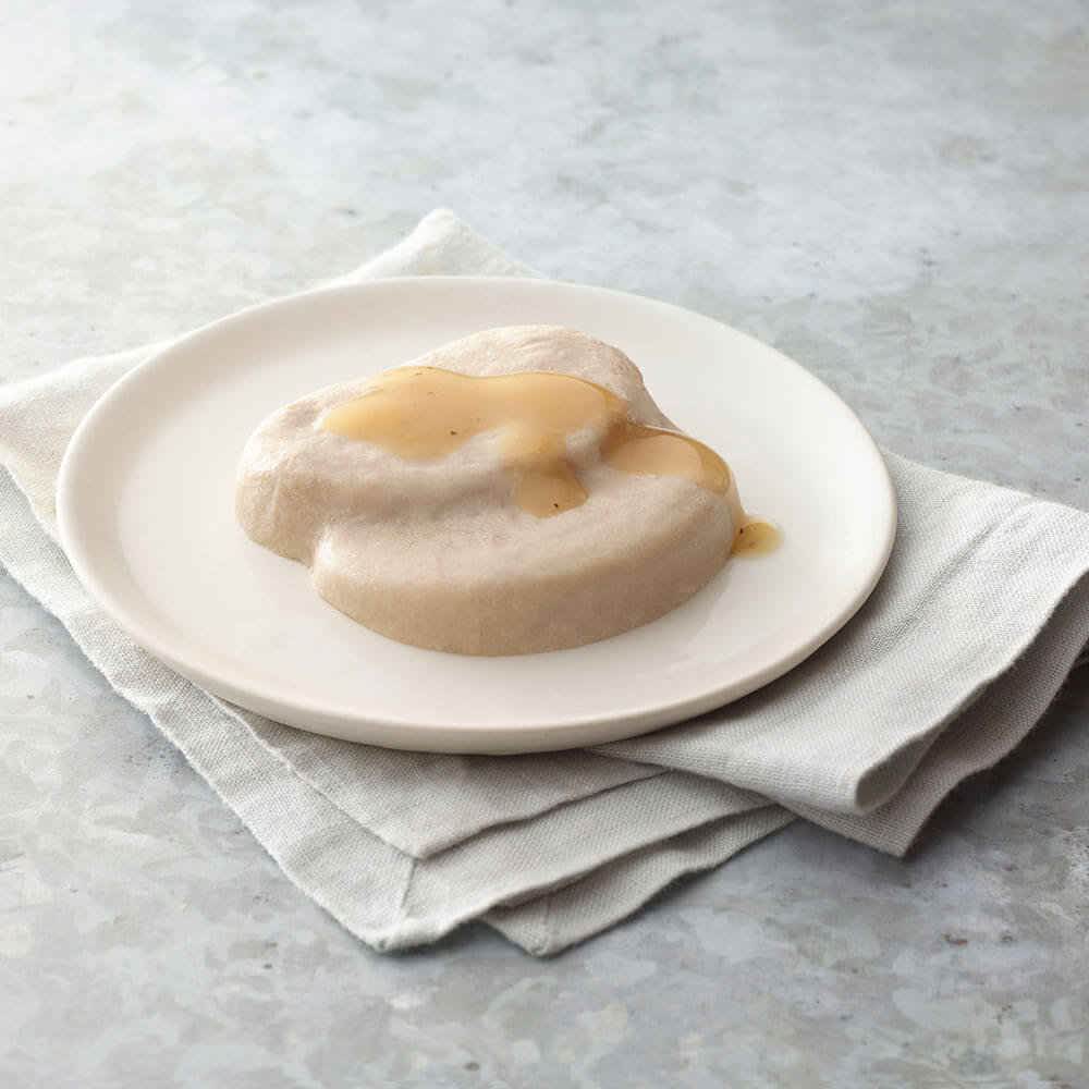 Mashed roast turkey with gravy on a white plate on a light gray surface.