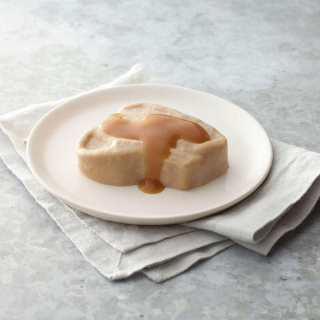 Roast pork with a caramel sauce on a white plate on a light gray surface.