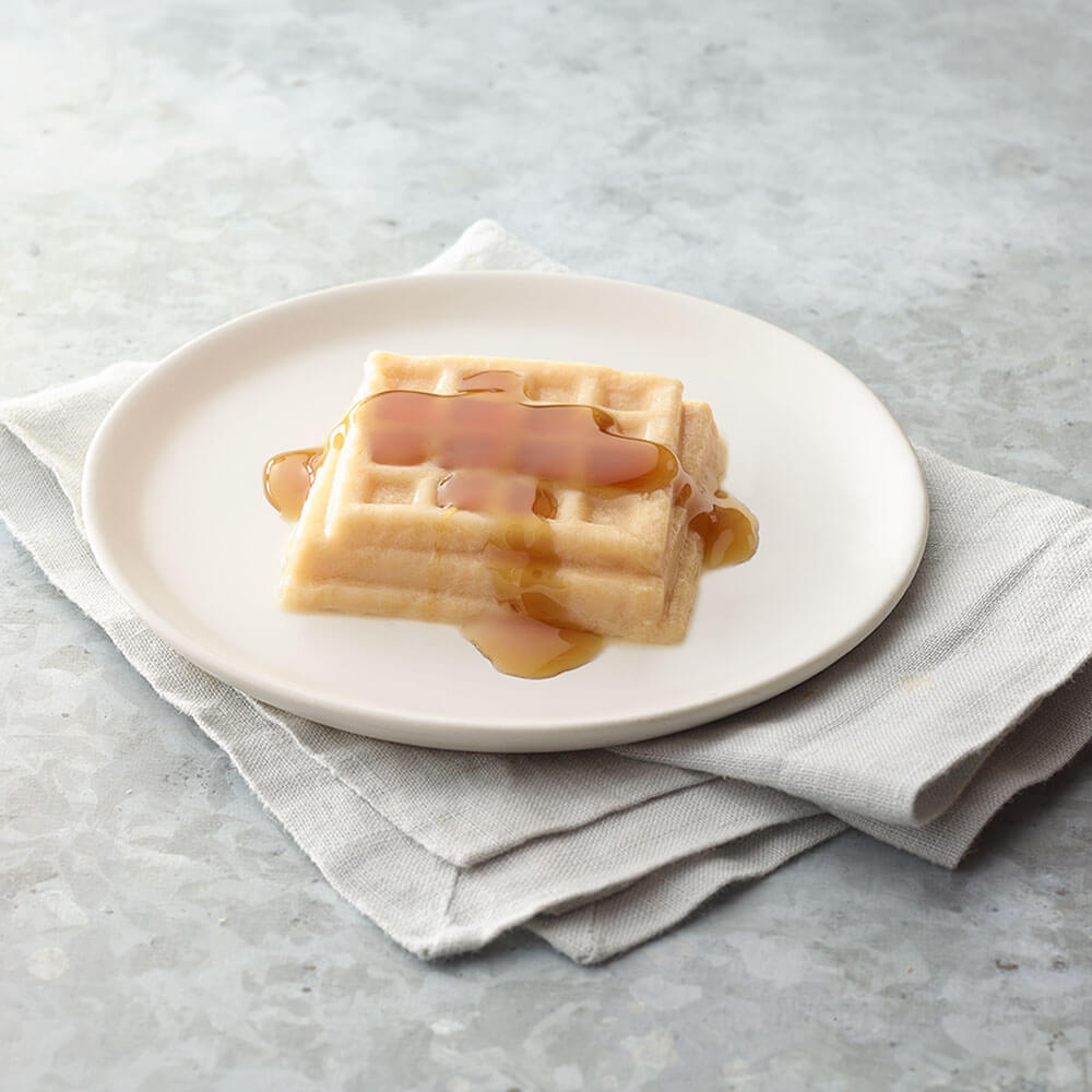 Waffles with syrup on a white plate on a gray surface.